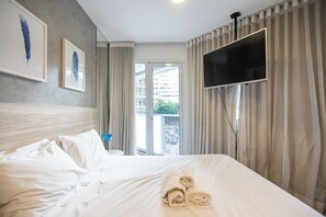 Habitación de hotel con cama, televisor montado en la pared y vistas al exterior a través de una ventana.