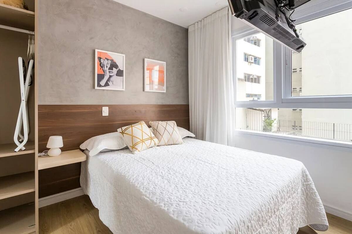 Habitación de hotel con una cama, una mesita de noche, una lámpara y dos cuadros en la pared.
