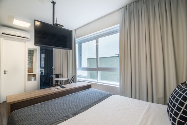 Habitación de hotel moderna con una cama grande, un televisor de pantalla plana en la pared, un escritorio con silla y una ventana con cortinas.