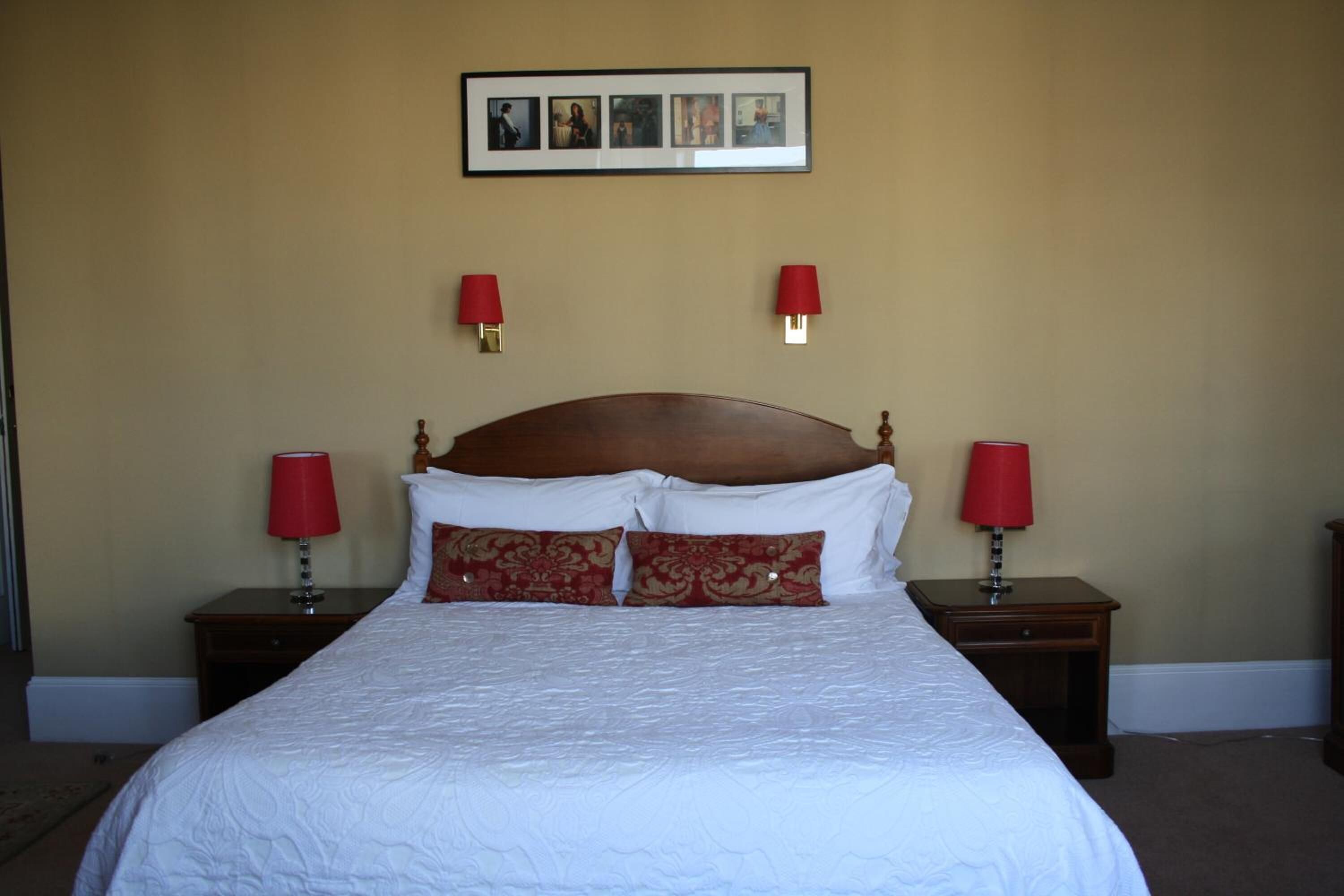 A neatly made bed with white bedding and two red lamps on either side.