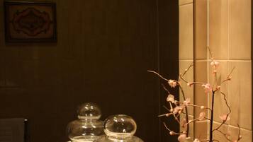 A bathroom with a granite countertop, a mirror, and a vase with a branch of pink flowers.