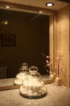 A bathroom with a granite countertop, a mirror, and a vase with a branch of pink flowers. - 17 Wilmington Square (Eastbourne)