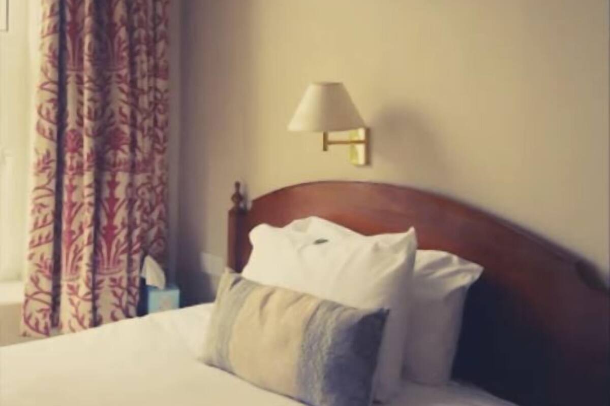 Ein Hotelzimmer mit einem Bett, einem Nachttisch, einer Lampe und einem Fenster mit Vorhängen.