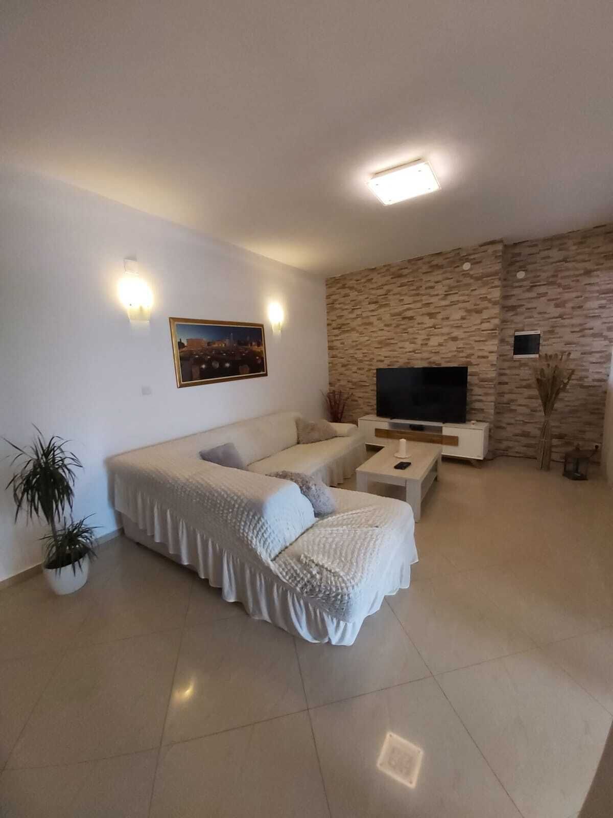 Un salon moderne avec un ensemble de canapés, un téléviseur à écran plat et un mur décoré d’un motif imitant la pierre.