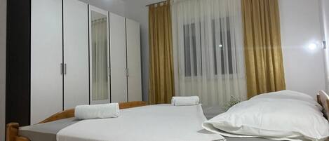 Une chambre à coucher avec un lit en bois, du linge de lit blanc, une table de chevet avec une télécommande et une armoire aux portes miroir.