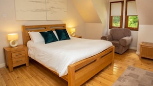 Una camera da letto con un letto di legno, due comodini con lampade, una sedia e una finestra vista verde.