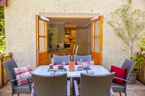 Un patio descubierto con una mesa dispuesta para dos, con sillas de mimbre y una botella de champán.