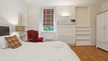 A bedroom with a bed, a red armchair, a window with a plaid curtain, a radiator, and a wardrobe.