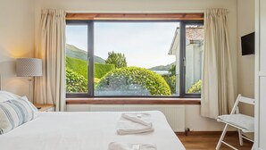 A hotel room with a large window, a bed, a chair, a lamp, and a radiator.