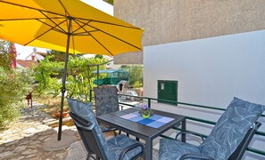 Un patio al aire libre con una mesa, sillas, un paraguas amarillo y vista a un edificio con una puerta verde.