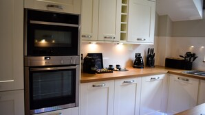 Una cocina moderna con armarios blancos, horno empotrado, cafetera y encimera de madera.