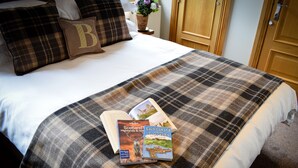 Una cama bien hecha con una colcha de cuadros, dos libros titulados 'Scotland's Highlands & Islands' y 'Loch Lomond and the Trossachs' de Caroline Hewitt, y un almohadón con una 'B' grande.