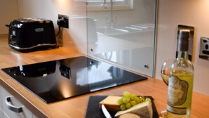 Una cocina con un tostador negro, una tabla de cortar con queso y uvas, y una botella de vino blanco.