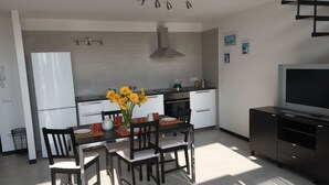 A modern kitchen with a dining area, featuring a central island with chairs, a refrigerator, a stove, and a television on a cabinet. - SweetHomeToledo Historical Center (Napoli)