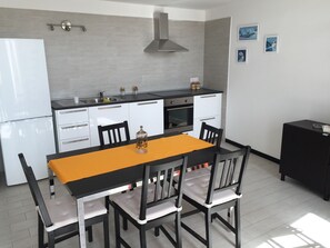 A modern kitchen with a dining table, chairs, a refrigerator, oven, and a black cabinet.