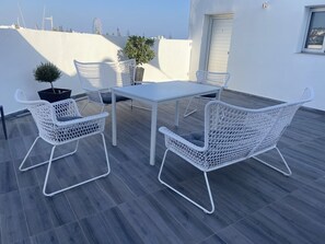En tagterrasse med et hvidt bord og stole, plantekasser og udsigt over byens skyline.