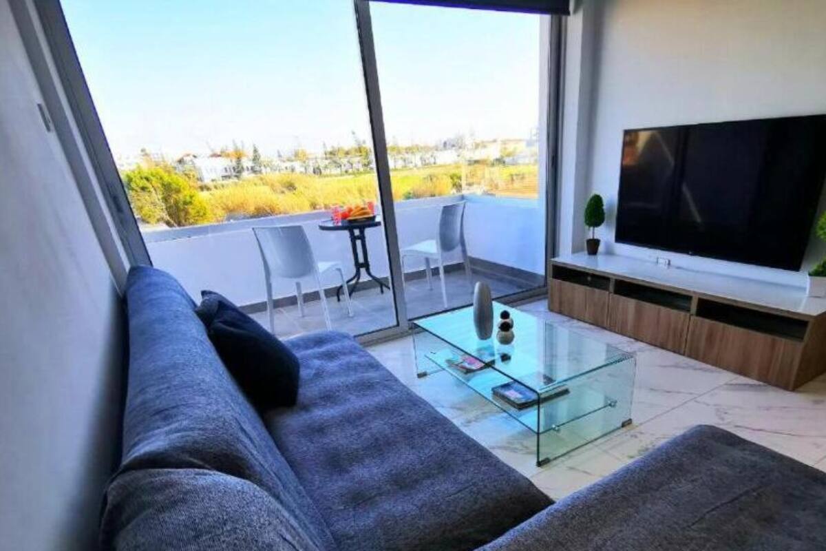 Uma sala de estar moderna com um sofá, uma mesa de centro de vidro e uma TV de tela plana.