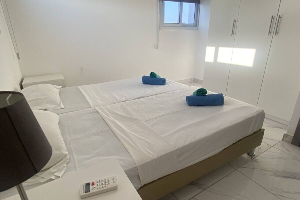 Quarto de hotel com duas camas, uma escrivaninha com abajur, um controle remoto e uma janela.