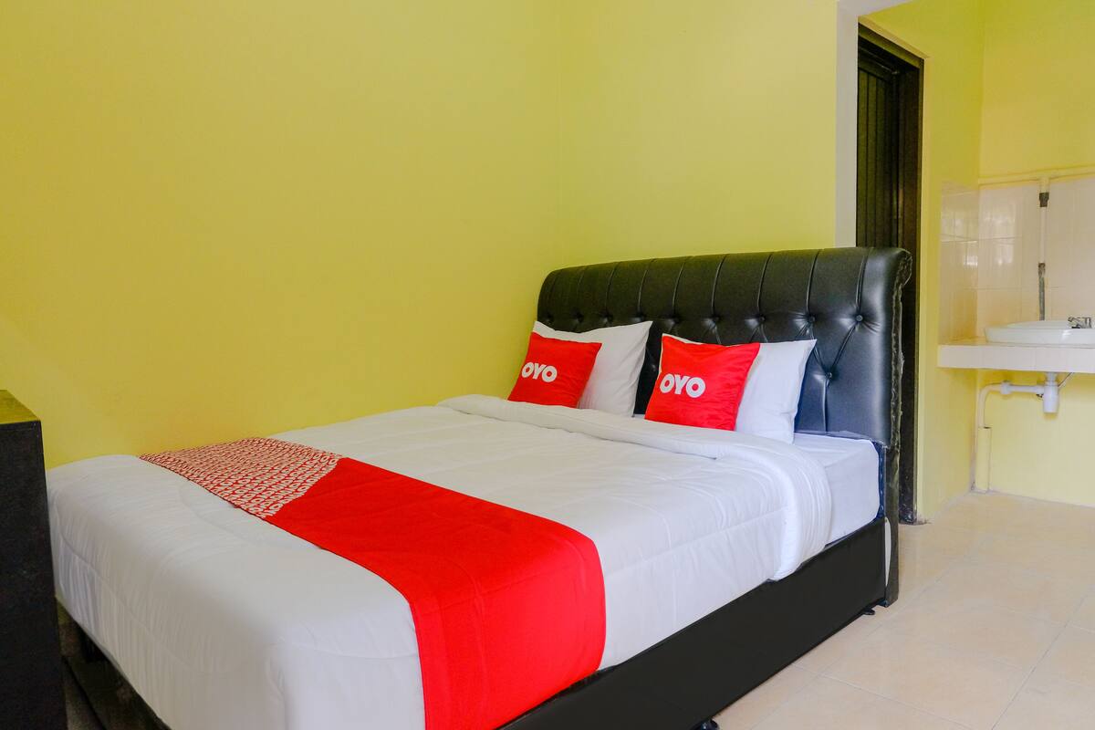 Un lit avec une tête de lit noire, une literie blanche et des touches de couleur rouge.