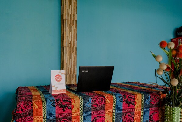 Una laptop sobre una mesa con mantel estampado, pared de bambú y un florero con flores.