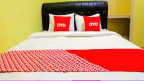 Een bed met een zwart hoofdbord, twee rode kussens met de tekst 'OYO', een wit sprei en een rood-wit geborreld deken.