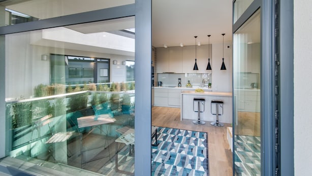 A modern kitchen with a central island, pendant lights, and a glass door leading to a balcony with a view of the outdoors.