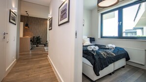 A modern hotel room with a large bed, a view of the city, and a hallway leading to a dining area.