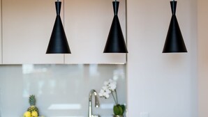 A kitchen with three black pendant lights, a sink, and a bowl of fruit on the counter.