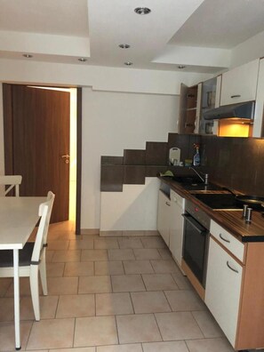 A compact kitchen with a dining area, featuring a wooden door, white cabinets, a stove, and a tiled floor. - Hotel Isabella (Frankfurt)