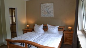 A bedroom with a wooden bed, two bedside tables with lamps, a door leading to a bathroom, and a wall-mounted artwork.