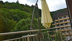 A balcony with a metal railing overlooking a lush green hillside and a building with multiple balconies.