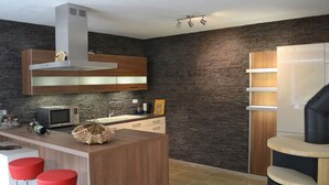 A modern kitchen with a central island, red bar stools, and a stone backsplash.