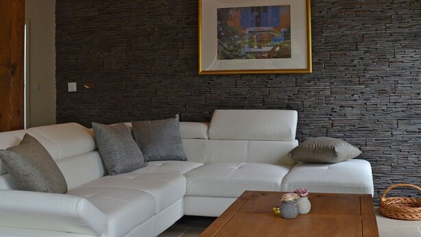 A modern living room with a white sectional sofa, a wooden coffee table, and a stone wall.