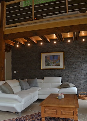 A modern living room with a white sectional sofa, a wooden coffee table, and a stone wall. - Ferienwohnung Panorama (Bad Bertrich)