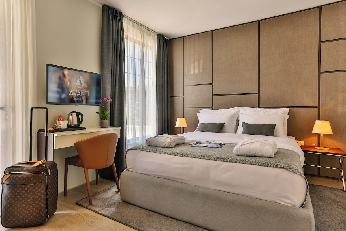 Une chambre d’hôtel avec un grand lit, un bureau, une chaise, une valise et un téléviseur fixé au mur.