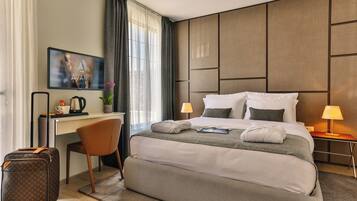 Quarto de hotel com uma cama grande, uma mesa, uma cadeira, uma mala e uma televisão na parede.