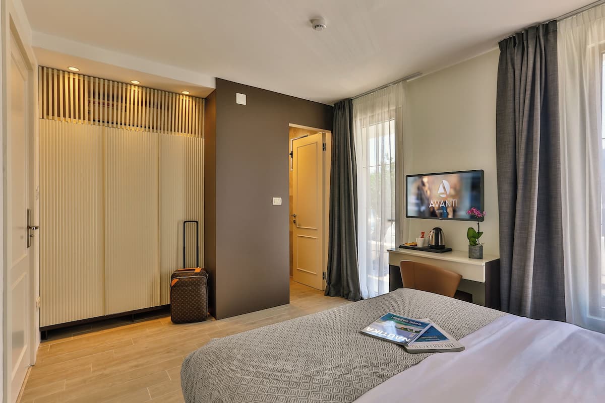 Une chambre d’hôtel avec un lit, un bureau, une télévision, une valise et une armoire.