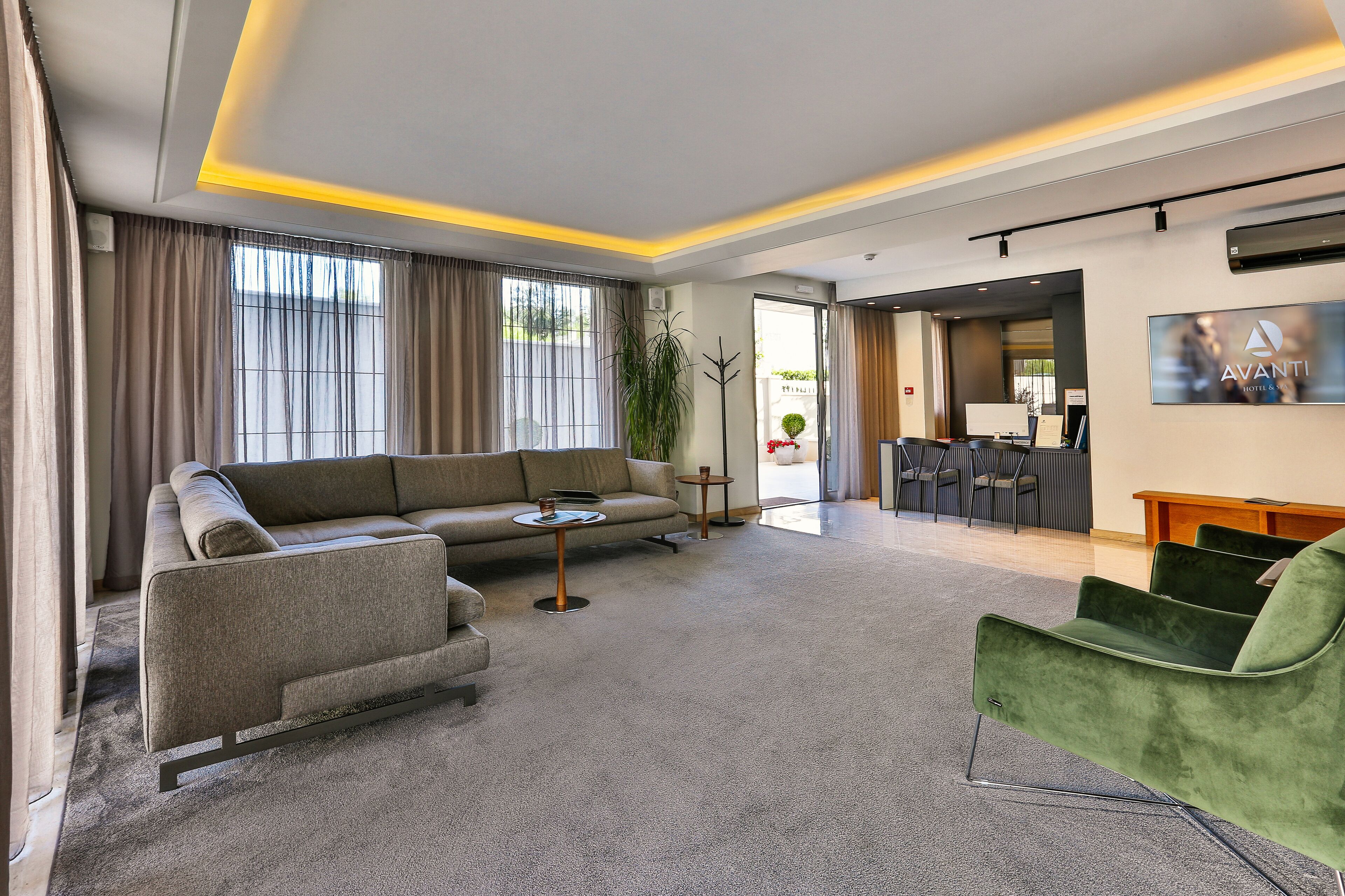 A modern hotel room with a grey sofa, a green armchair, and a small table.