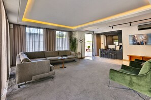 Una habitación de hotel moderna con un sofá gris, un sillón verde y una pequeña mesa.