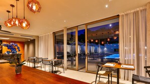 Un comedor moderno con una mesa de madera, sillas y vistas a una piscina exterior de noche.