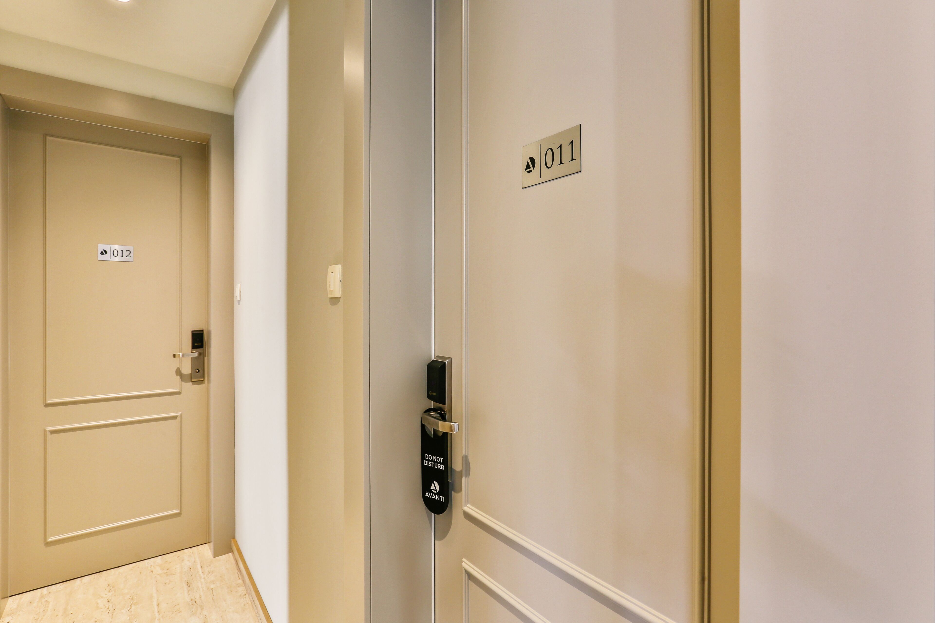 A hotel corridor with doors labeled 011 and 012, a do-not-disturb sign, and a modern door handle.