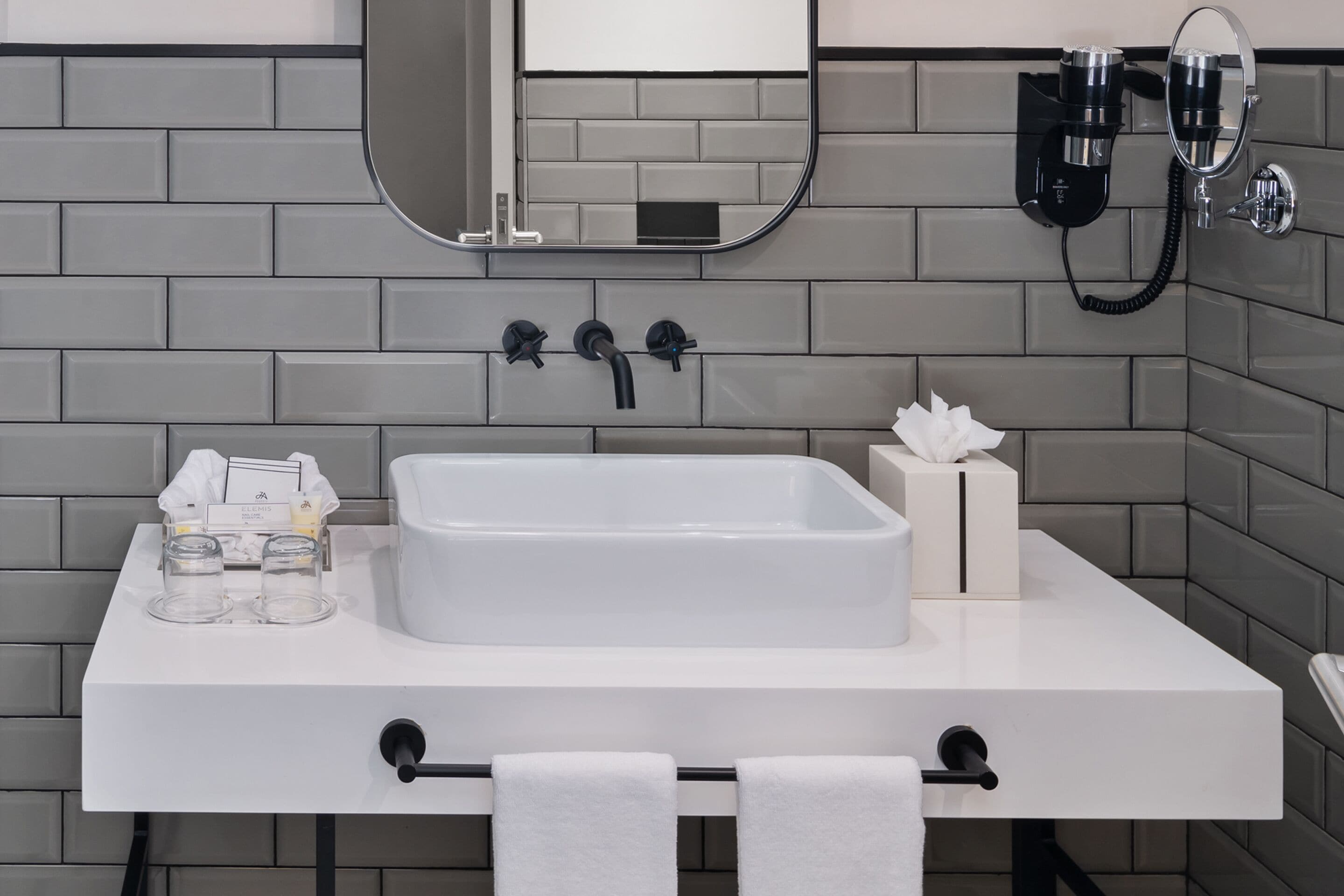 Un bagno moderno con un lavandino bianco, uno specchio e un asciugacapelli fissato alla parete.