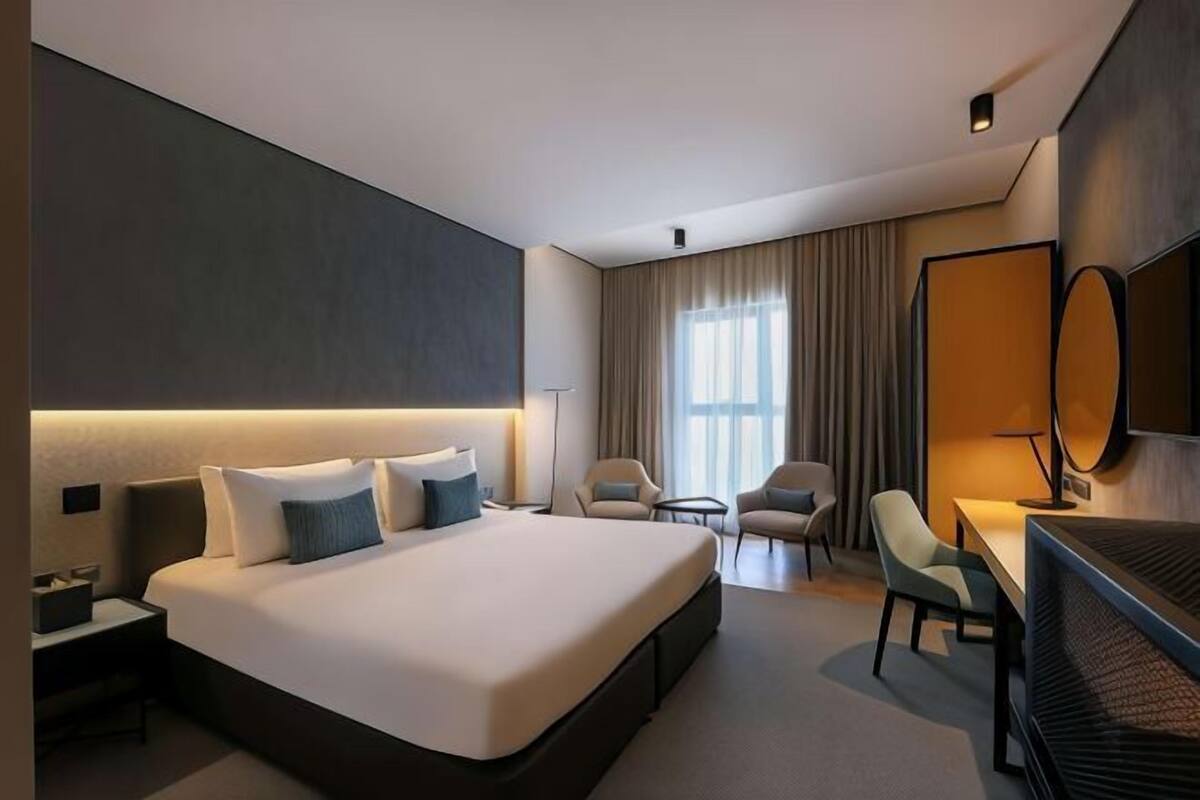 A modern hotel room with a large bed, a desk, a chair, and a TV.