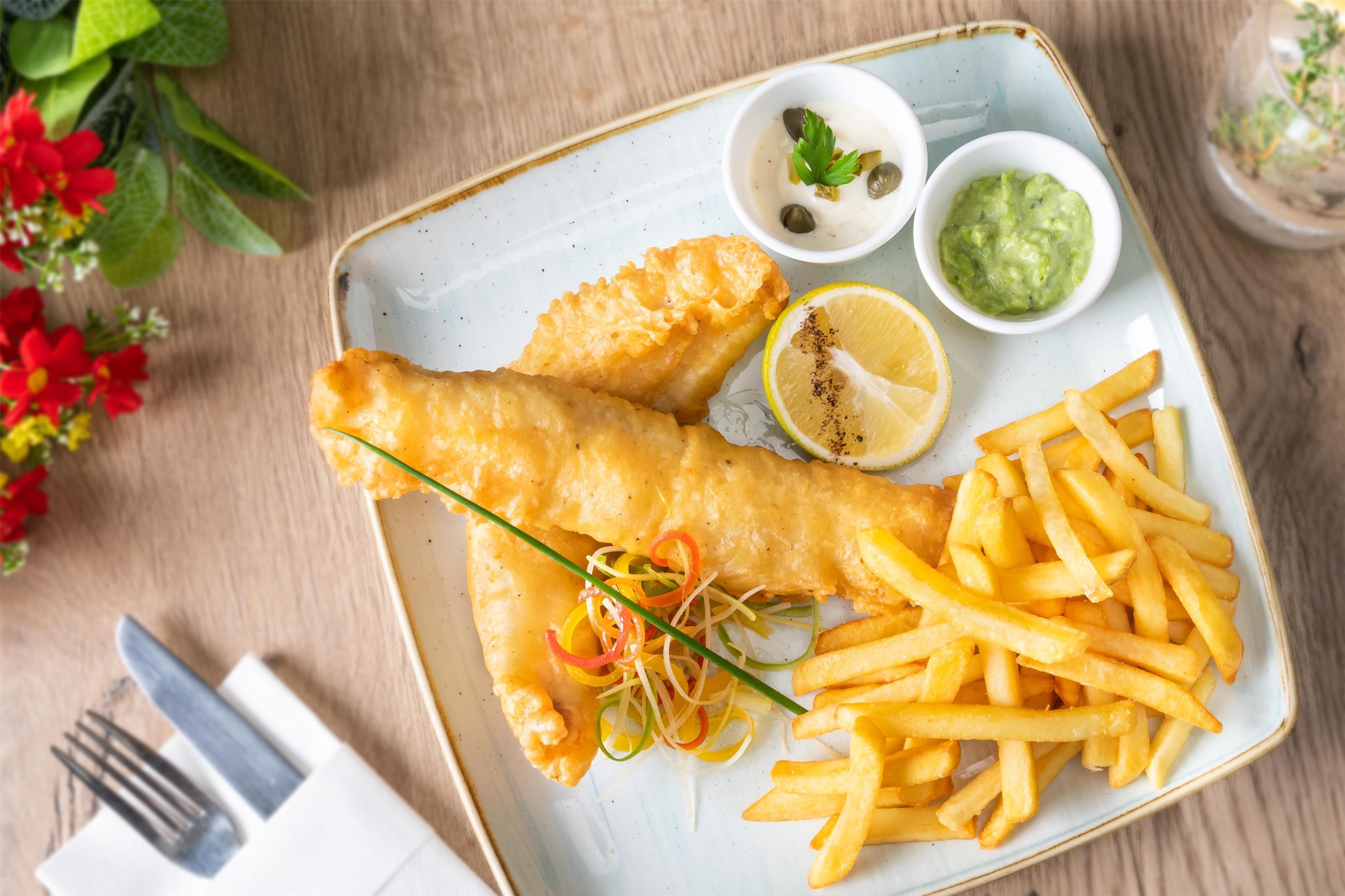 Ein Teller Fish and Chips mit Zitronenspalten, Tartarsauce und Erbsenpüree.