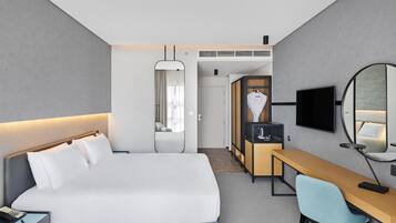 A modern hotel room with a large bed, a desk, a chair, a TV, and a wardrobe.