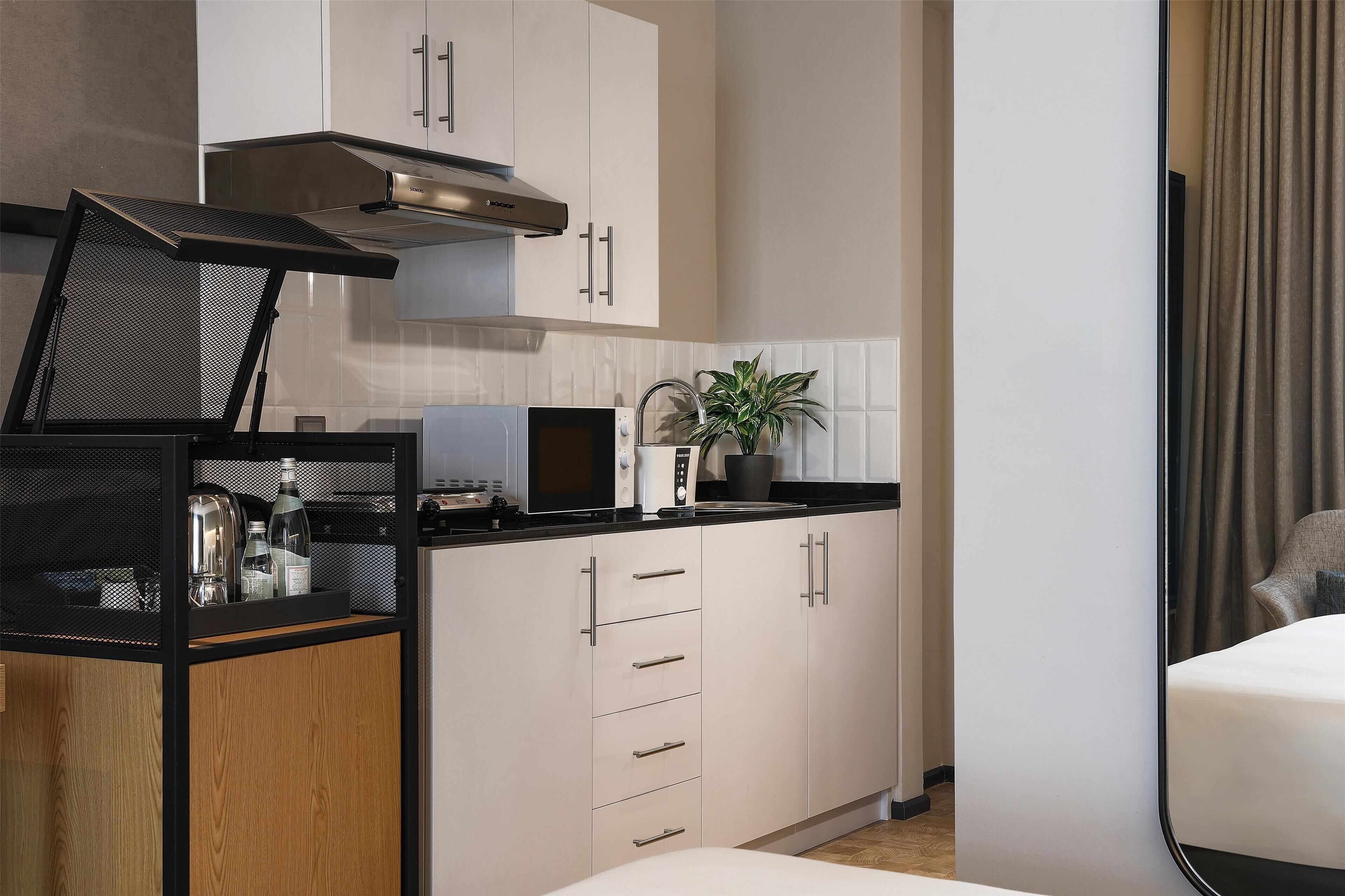 Eine kompakte Küche mit Mikrowelle, Toaster und Kaffeemaschine auf der Arbeitsfläche, einer Edelstahl-Dunstabzugshaube darüber und einem Topf mit Pflanze auf der Arbeitsfläche.