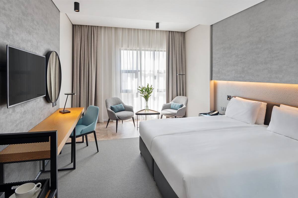 A modern hotel room with a large bed, a desk with a chair, a TV, and a small table with a plant.