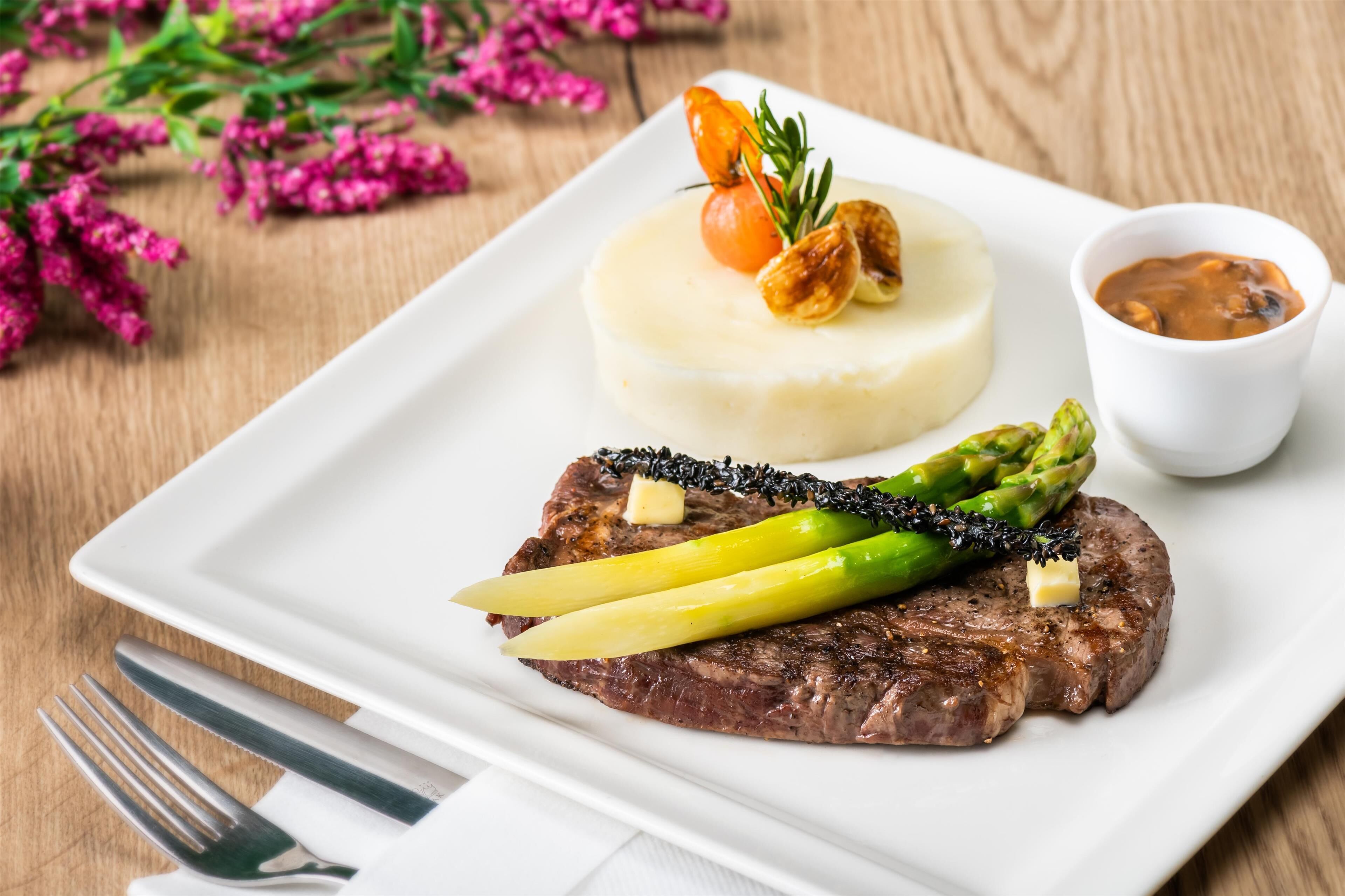 A plate with steak, asparagus, mashed potatoes, and a small bowl of sauce.