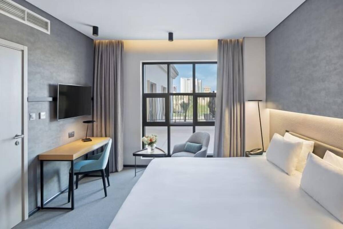 A hotel room with a bed, a desk, a chair, a TV, and a window with curtains.