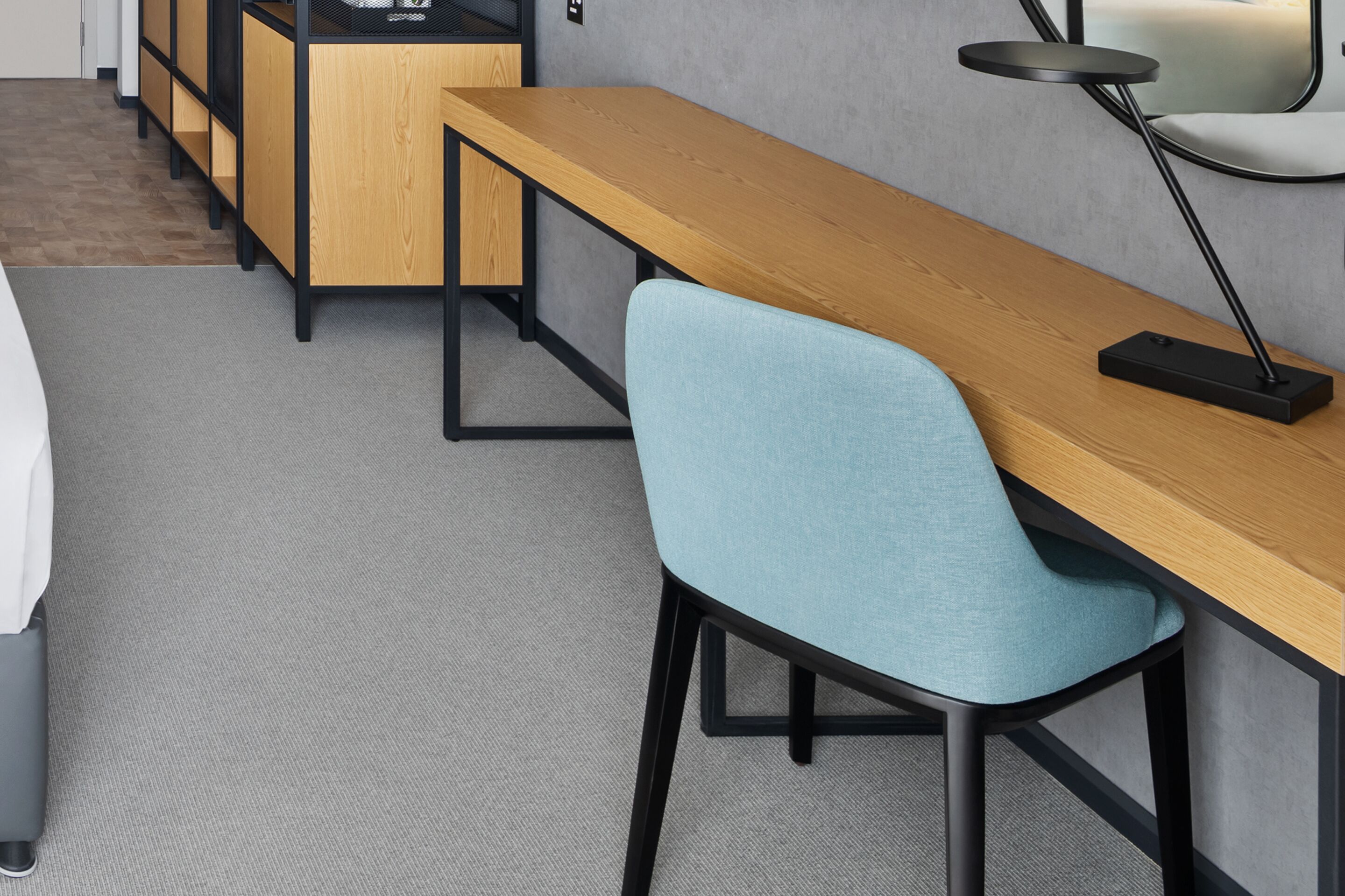 Una habitación de hotel moderna con un escritorio de madera, una silla azul, una mesita pequeña y una lámpara.